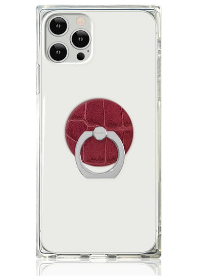 Burgundy crocodile textured circular phone ring stand with silver metal loop attached to clear protective phone case.