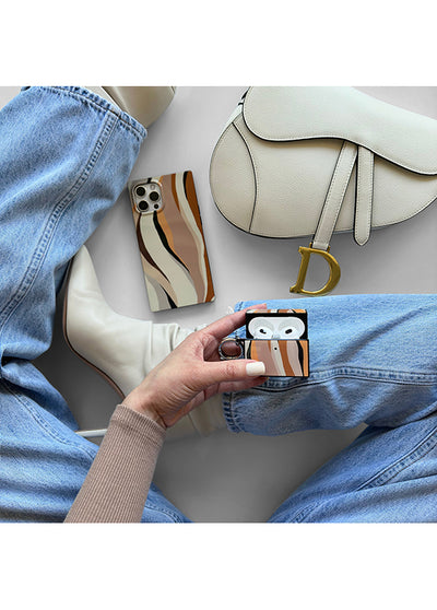 AirPods case with tan, brown, and cream horizontal stripes held in hand, displaying white earbuds inside.