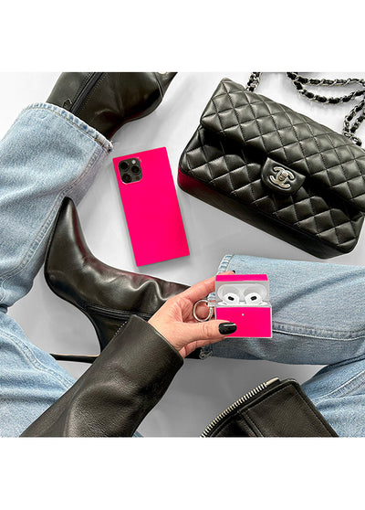 Bright neon pink square-shaped AirPods case with keychain, held in hand next to luxury accessories.