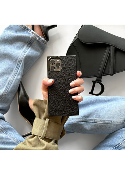 Black faux leather iPhone case with textured ostrich pattern held in hand, showing camera cutout and square shape.