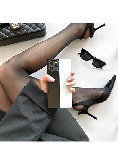 Black and white colorblock iPhone case with vertical split design, held in hand showing camera lens cutout.