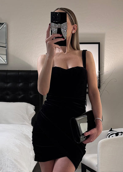 Black iPhone case with sparkly bow design on back, held by person in mirror selfie.
