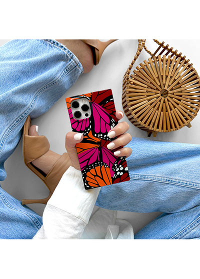 Square phone case with pink, orange, and red butterfly wings pattern held in hand.