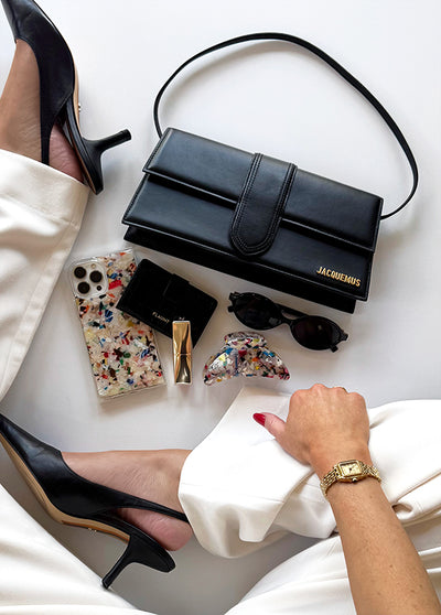 Tortoise shell claw clip with rainbow confetti pattern displayed among lifestyle items including black heels, wallet, and sun