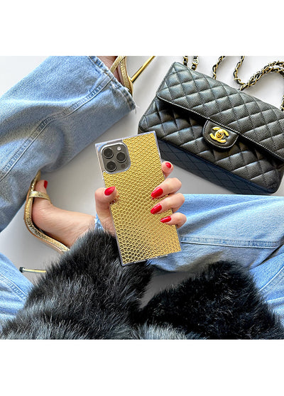 Gold snakeskin textured iPhone case held in hand with red nail polish, styled with denim and accessories.