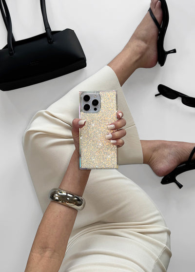 Square iPhone case with iridescent crystal glitter finish and silver metal frame held in hand.