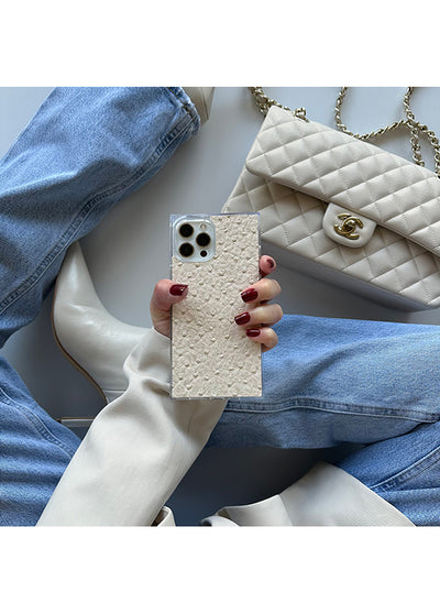 Ivory faux leather iPhone case with textured ostrich pattern and square shape, held in hand with dark red nail polish.