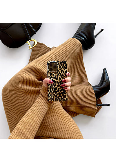 iPhone case with black and cream leopard print pattern and gold-tone hardware, held in hand.