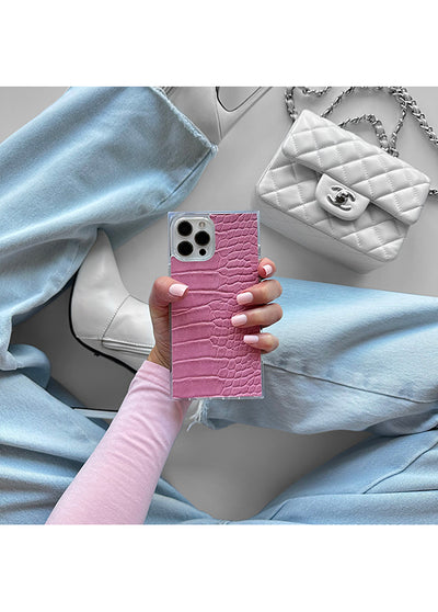 Pink crocodile-textured faux leather iPhone case with square shape, held in hand showing camera cutout and silver metal frame