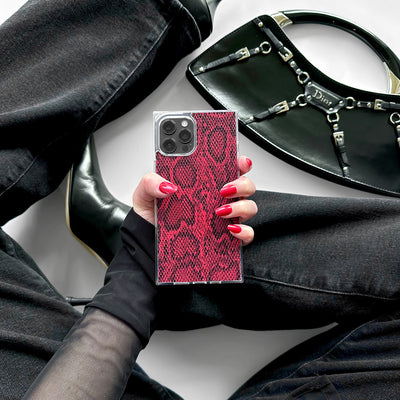 Red python textured iPhone case with silver camera ring held in hand with black accessories nearby.