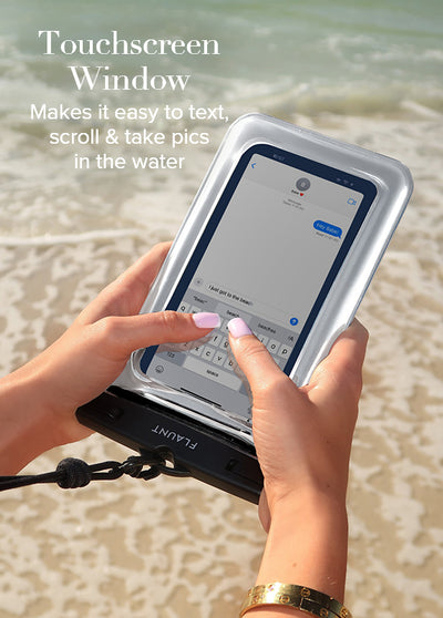 Silver waterproof phone pouch with clear touchscreen window held in hands at beach.