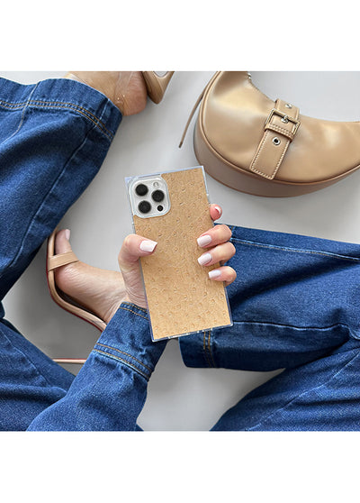 Tan ostrich faux leather iPhone case with square shape, held in hands next to matching tan shoe.