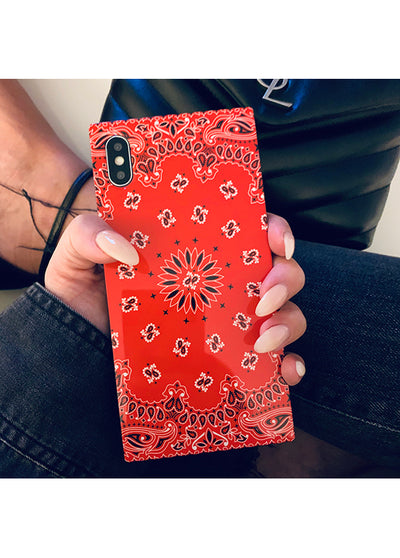 Red iPhone case with white bandana pattern and decorative floral motifs held in hand.