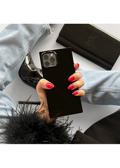 Black patent iPhone case with square shape held in hand, showing camera cutout and glossy finish.