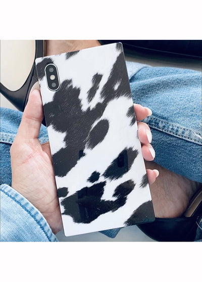 Black and white cow print iPhone case held in hand, showing spotted pattern and dual camera cutout.