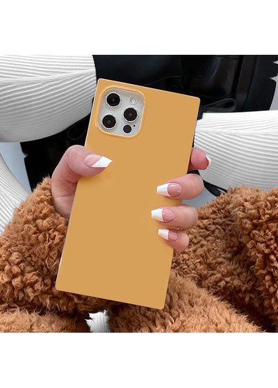 Honey-colored square iPhone case with camera cutout, held in hand showing nude and white manicure.