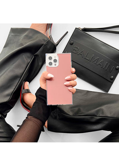 Rose pink square iPhone case with metallic silver camera cutout, held in hand against black accessories.