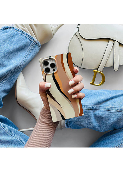 Beige iPhone case with brown and black vertical stripes, held in hand alongside a cream shoulder bag.