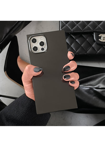 Black square iPhone case with metallic camera ring held in hand against quilted black handbag.