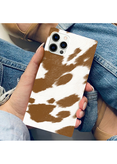 Tan and white cow print iPhone case with square shape and triple camera cutout, held in hand.