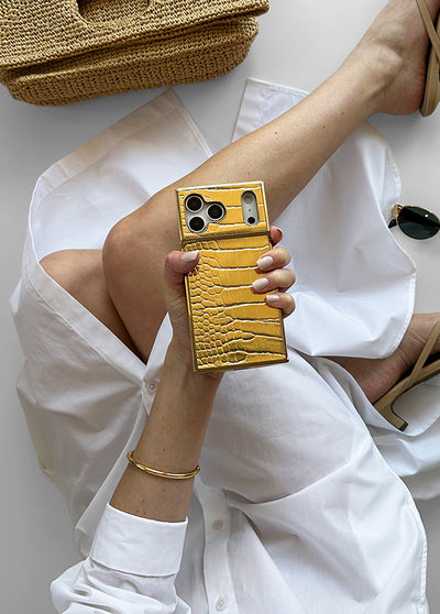Gold textured iPhone case with crocodile pattern held in hand, showing dual camera cutout and square shape design.