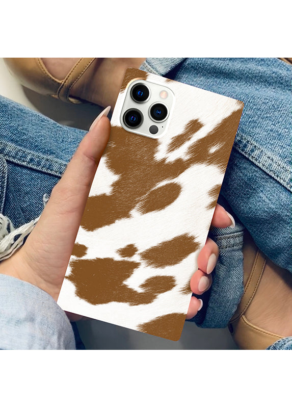 Tan and white cow print iPhone case with square shape and triple camera cutout, held in hand.